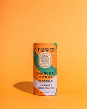 A cylindrical Charcoal Citrus Deodorant Plastic-Free Tube by Good Flower Farm is shown on an orange background. The green, orange, and white biodegradable tube is aluminum- and baking soda-free.