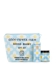 The Good Baby Gift Set by Good Flower Farm includes a blue cosmetic bag with white and yellow floral designs, plus a matching box and jar, featuring baby diaper balm made with gentle botanical ingredients.