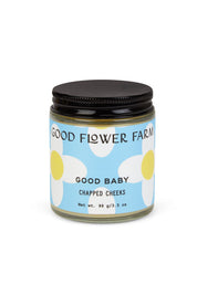 A glass jar from Good Flower Farms Good Baby Gift Set has a blue and white label with white flowers, a black screw-on lid, and is made with gentle botanicals; the jar contains 99g (3.5 oz) of baby diaper balm.