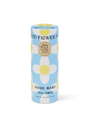 A cylindrical Good Flower Farm Good Baby Gift Set container sits on a blue background with white, yellow-centered flowers. Its label displays a gold emblem and black text, highlighting gentle botanical ingredients.