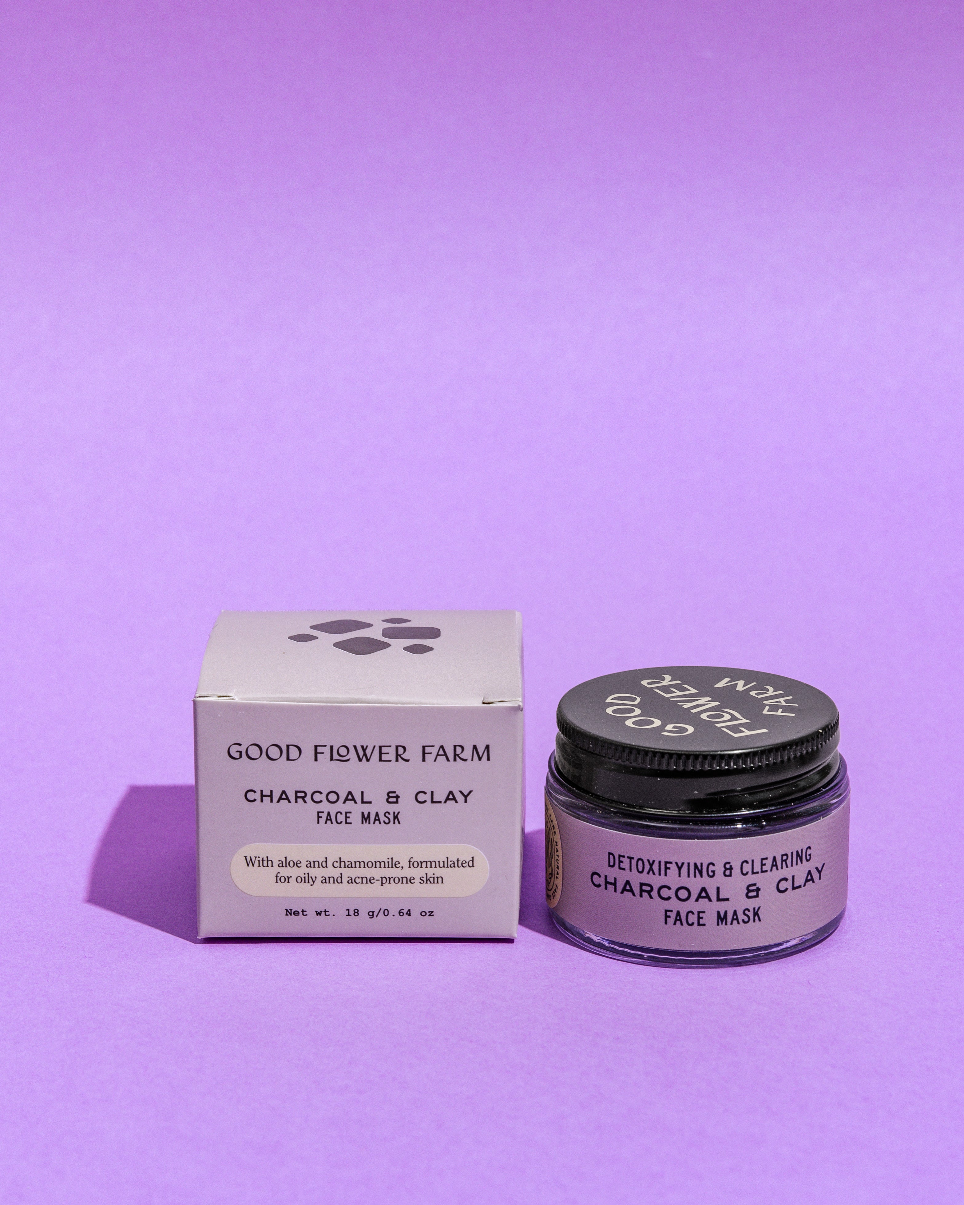 Good Flower Farm Charcoal & Clay Botanical Face Mask, in box and jar, is shown on a purple background. The labels feature detoxifying and nourishing ingredients like aloe, chamomile, bentonite clay, and activated charcoal.