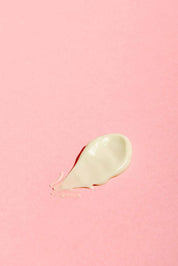 A dollop of Good Flower Farms Rose Geranium Face Cream is spread on a smooth, pastel pink background.