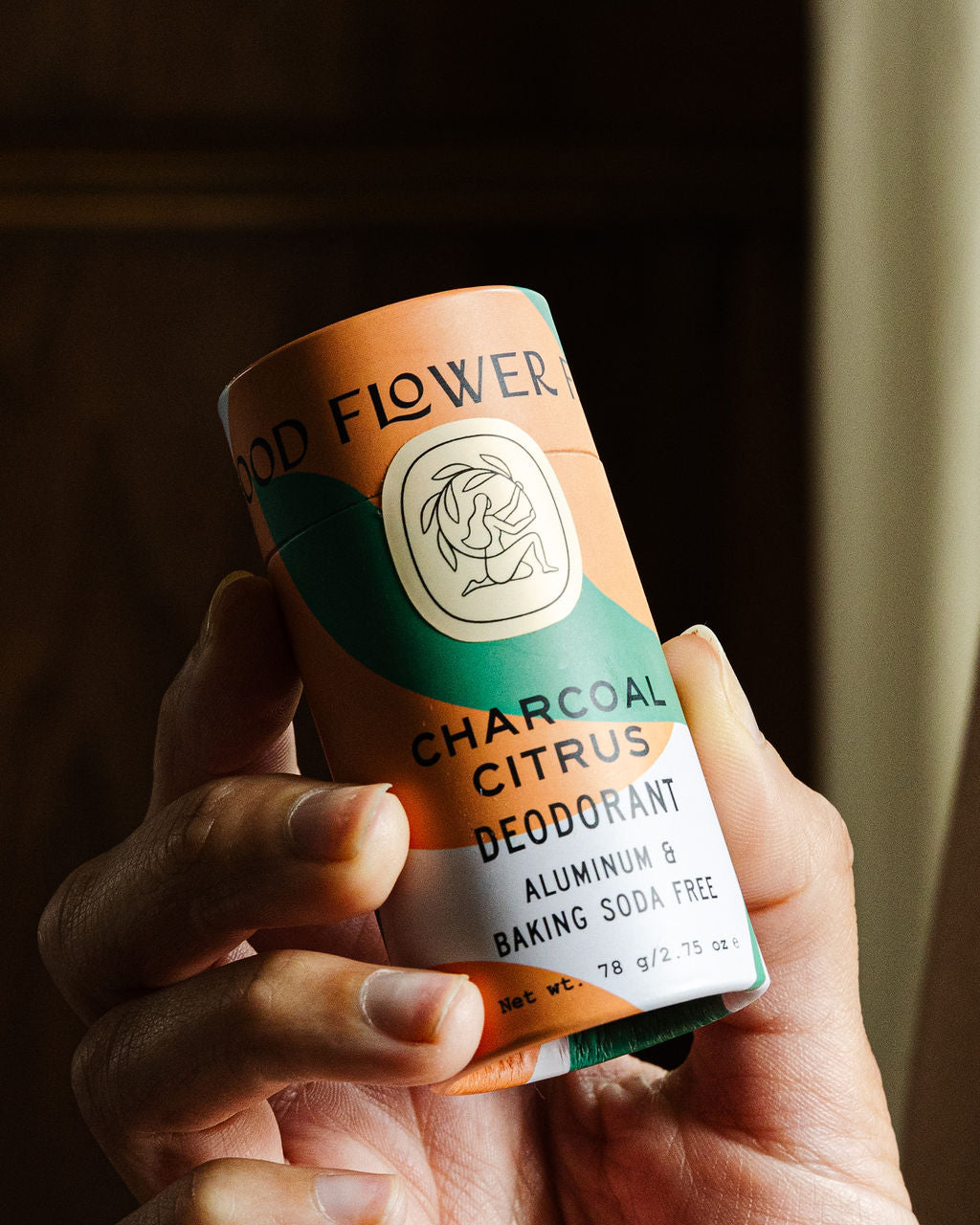 A hand holds a Good Flower Farm Charcoal Citrus Deodorant Plastic-Free Tube, aluminum and baking soda free, in a biodegradable tube against a softly lit background.