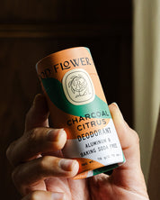 A hand holds a Good Flower Farm Charcoal Citrus Deodorant Plastic-Free Tube, aluminum and baking soda free, in a biodegradable tube against a softly lit background.
