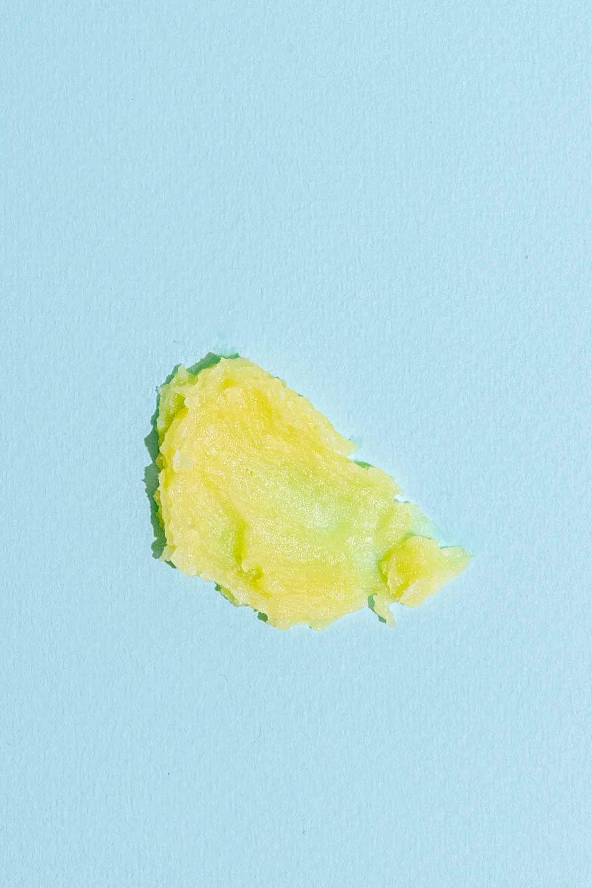 A dab of yellow and green Garden Salve by Good Flower Farm, crafted from farm-grown herbs, displayed on a light blue background.