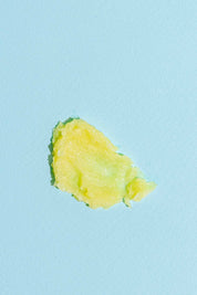 A dab of yellow and green Garden Salve by Good Flower Farm, crafted from farm-grown herbs, displayed on a light blue background.