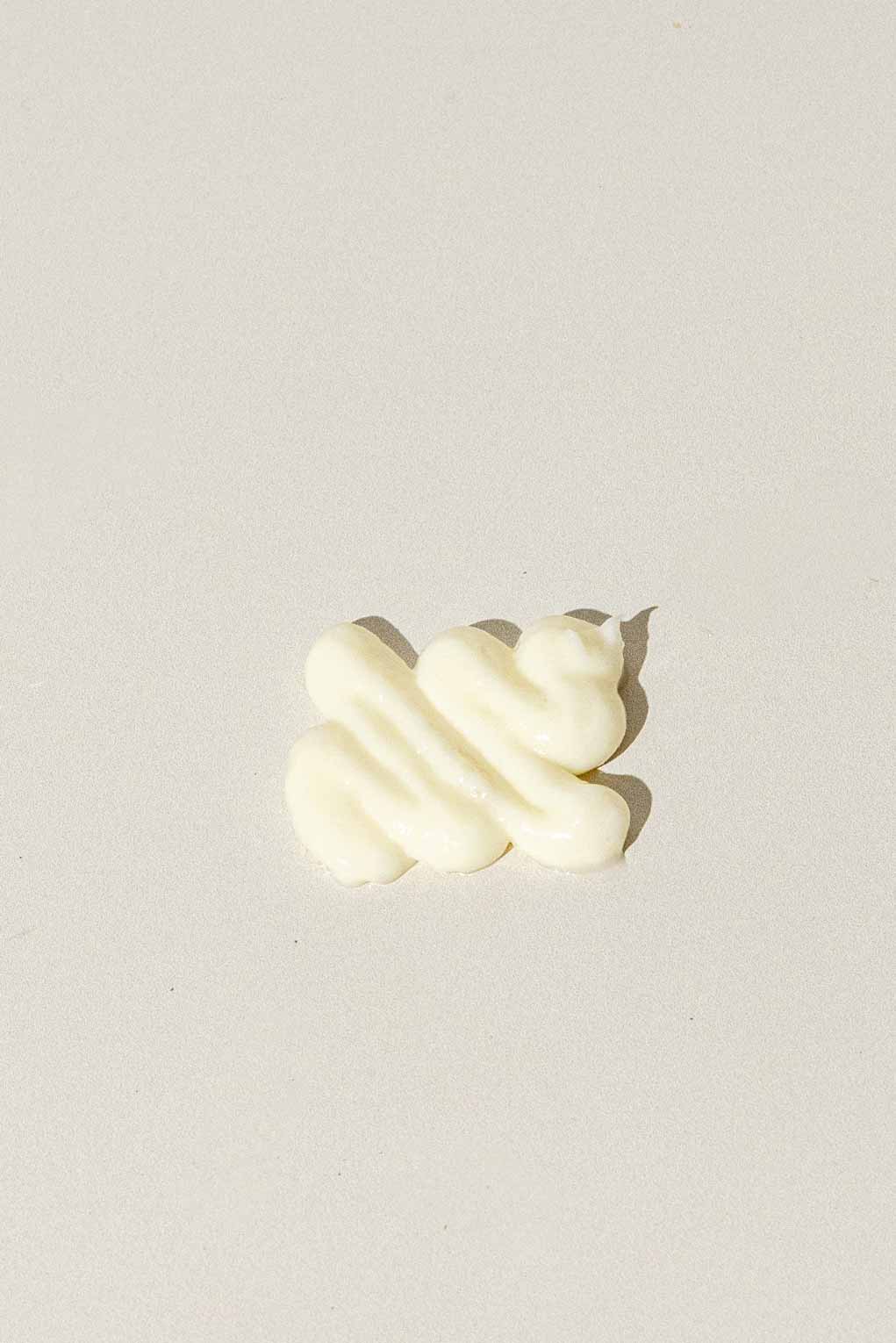 A small swirl of Good Flower Farm’s Herbal Enzyme Cream Cleanser & Makeup Remover rests on a light surface, suggesting gentle care powered by plant-based enzymes.