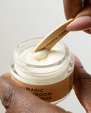 A person uses a Good Flower Farm Reusable Bamboo Spatula to scoop cream from a jar, with neatly manicured nails and the jar held in their other hand.