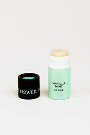A tube from the Good Flower Farm Rainbow Organic Lip Balm Set of 6 stands upright beside its black lid, both on a plain white background—ideal for moisturizing lips while staying eco-friendly.