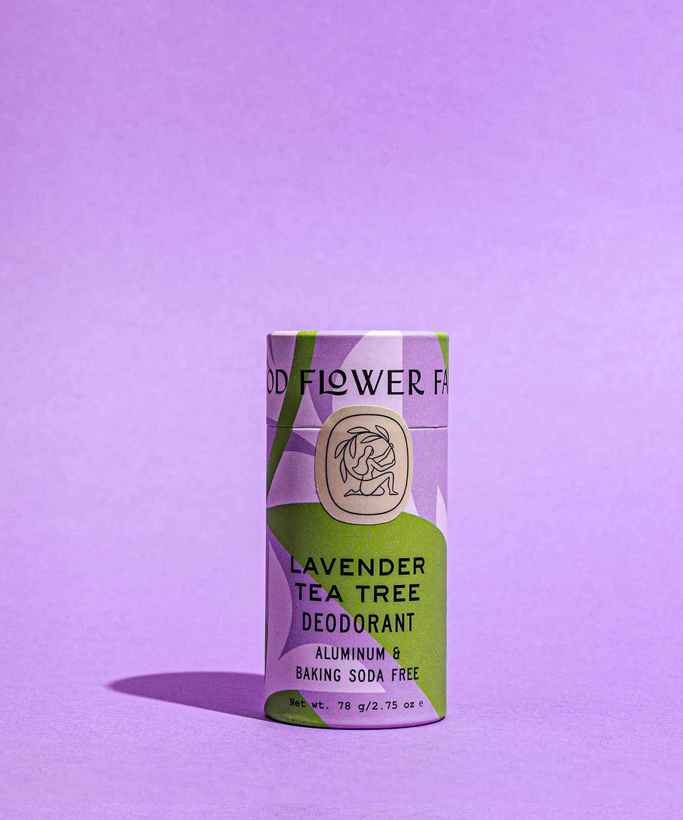 A Good Flower Farm Lavender Tea Tree Deodorant Plastic-Free Tube with a lavender and green design stands upright on a purple background; its aluminum-free packaging highlights that it’s baking soda free.