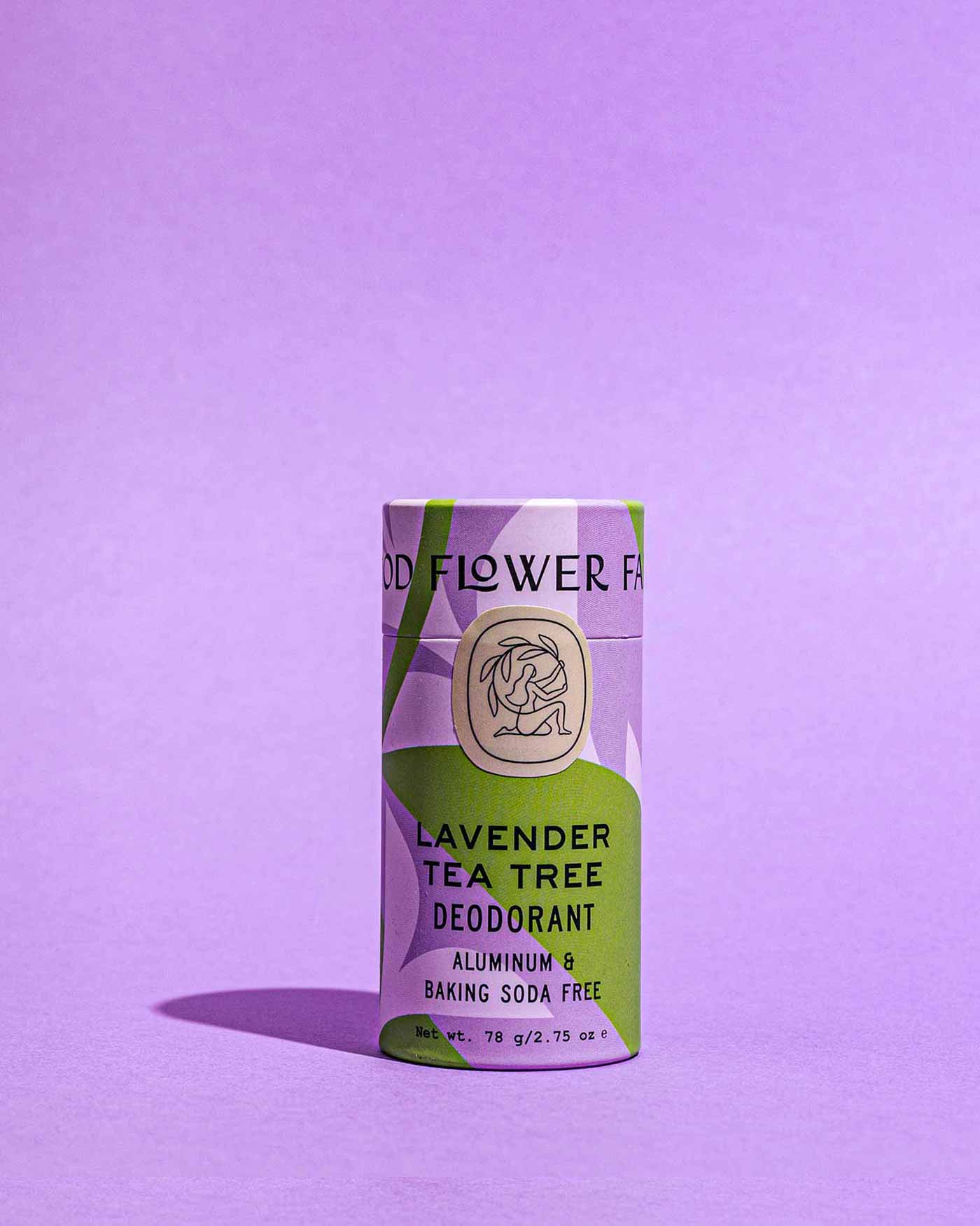 A Good Flower Farm Lavender Tea Tree Deodorant Plastic-Free Tube with a lavender and green design stands upright on a purple background; its aluminum-free packaging highlights that it’s baking soda free.