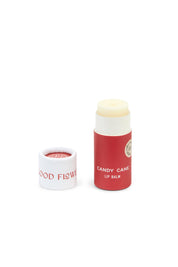 A red and white cylindrical tube of SEASONAL LIMITED Holiday Lip Gift Set - NEW by Good Flower Farm stands next to its removed cap. The eco-friendly, biodegradable packaging contains light-hued lip balm made with coconut oil.