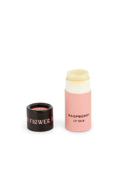 A pink tube of Good Flower Farm Seconds Lip Balm in raspberry, with the black cap featuring gold lettering placed beside it, stands out elegantly on a white background—proof that Seconds Lip Balm offers beautiful care inside.