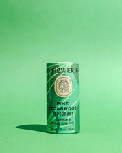 A green cylindrical tube of Good Flower Farm Pine Cedarwood Deodorant Plastic-Free stands upright on a matching background. The label notes its aluminum- and baking soda-free, in biodegradable packaging.